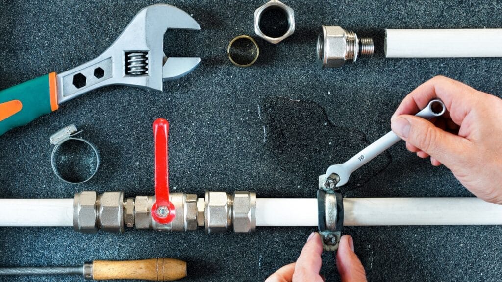 Plumber repairing a pipe valve with an adjustable wrench in Lawrenceville