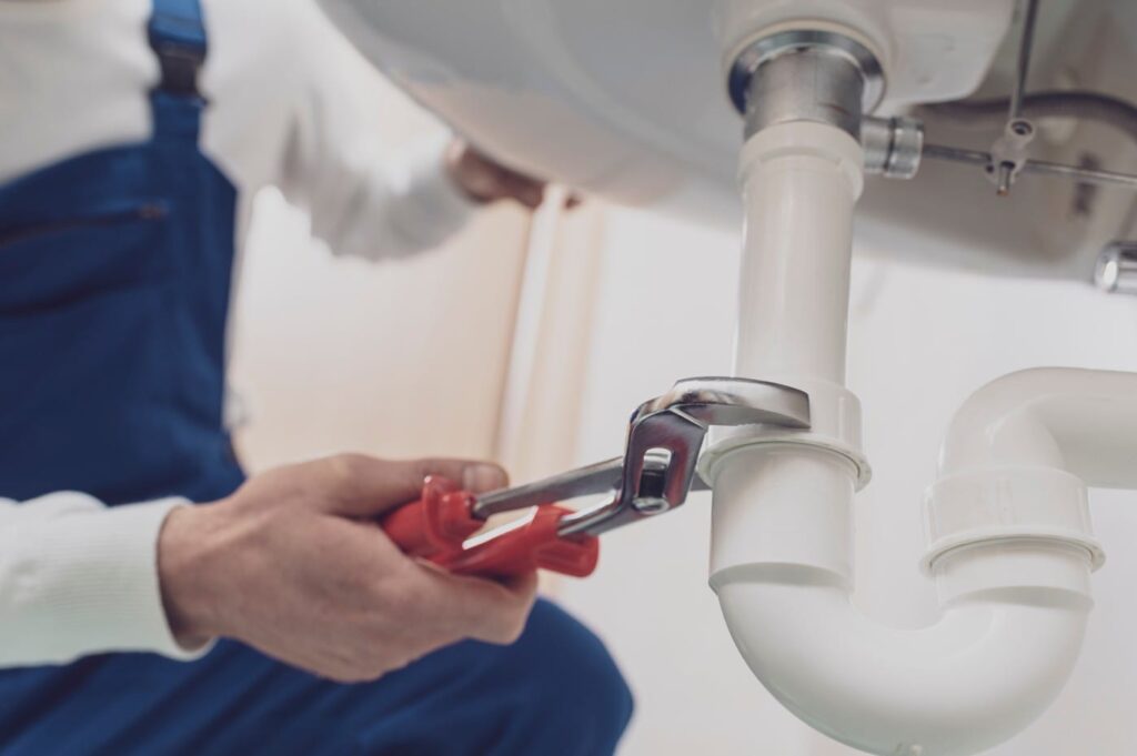 Plumber repairing a white drain pipe beneath a sink in Lawrenceville